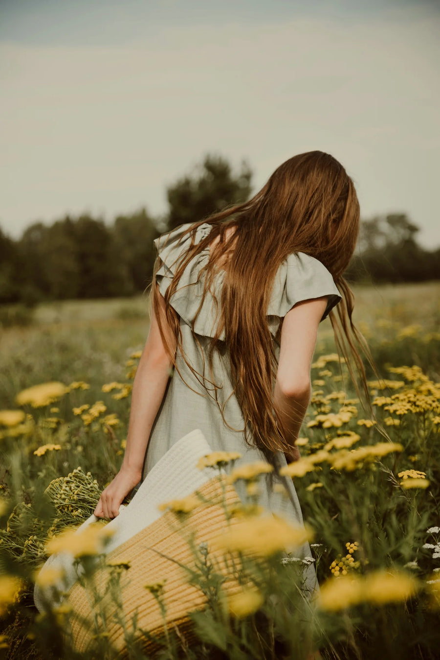 Woman with long hair seen from behind walking through a meadow of yellow flowers, photo by Anita Austvika