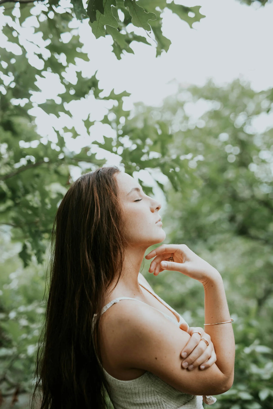 Woman with her eyes closed and her head tilted back in a green garden, photo by Brooke Cagle