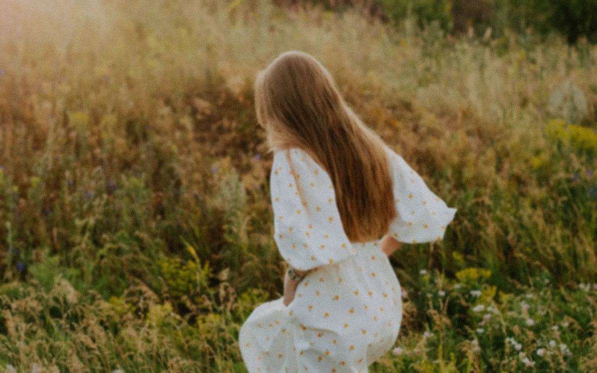 Woman in a white dress walking up a grassy hillside in warm light, softly blurred, photo by Kateryna Hliznitsova