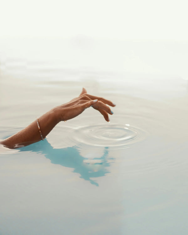Woman's arm reaching into still water, making ripples, photo by Daniela Matthies