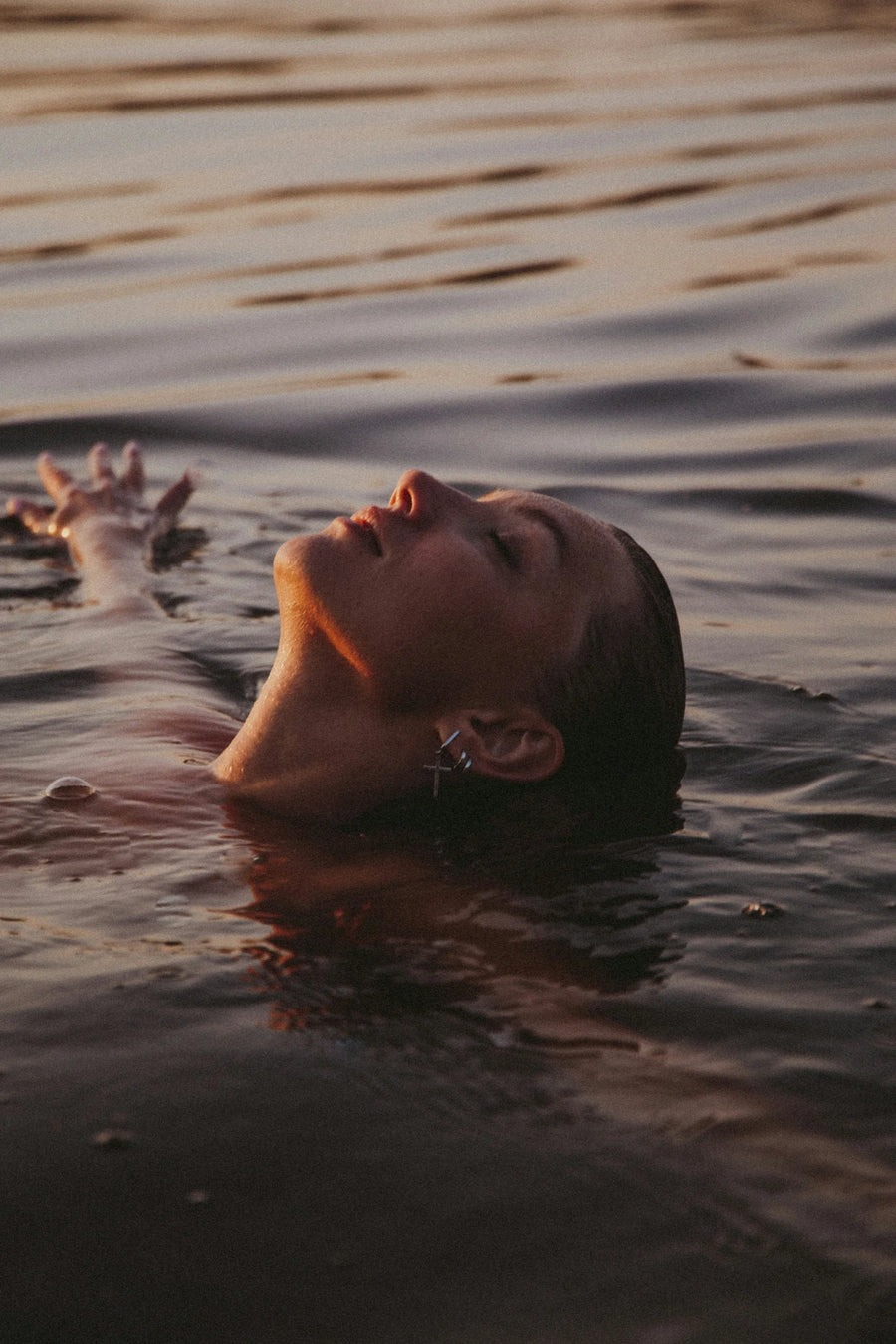 Woman with her head tilted back floating in calm water at sunset, photo by Klara Kulikova