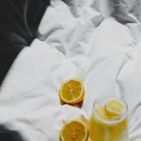 Lemon halves and a glass of lemon water on a white crumpled sheet, photo by Laura Chouette