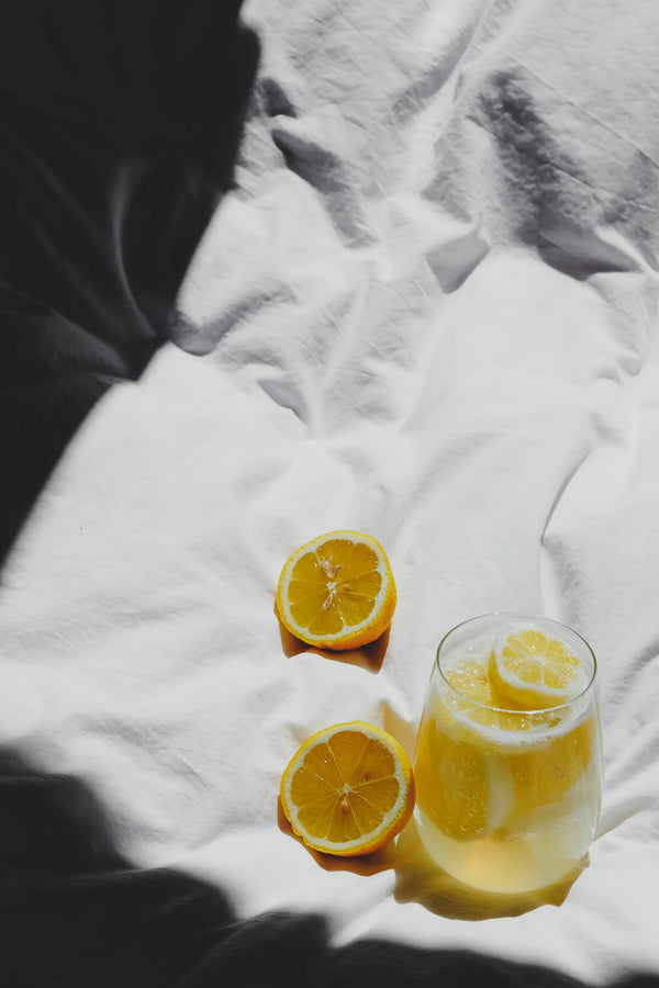 Lemon halves and a glass of lemon water on a white crumpled sheet, photo by Laura Chouette