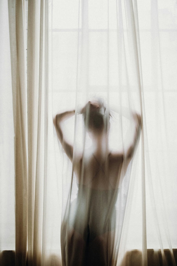 Silhouette of a person with their hands on their head behind a sheer curtain, photo by Monika Kozub