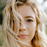 Nærbillede af en smilende blond kvinde med hår der blæser ind over ansigtet, foto af Rachel Mcdermott