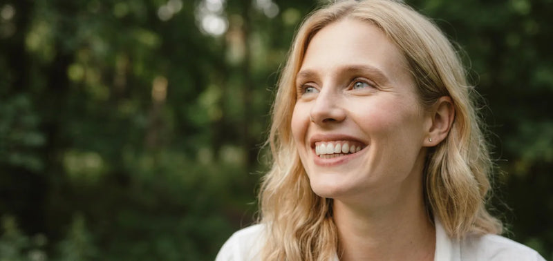 Smiling woman with blonde hair outdoors in a green forest setting