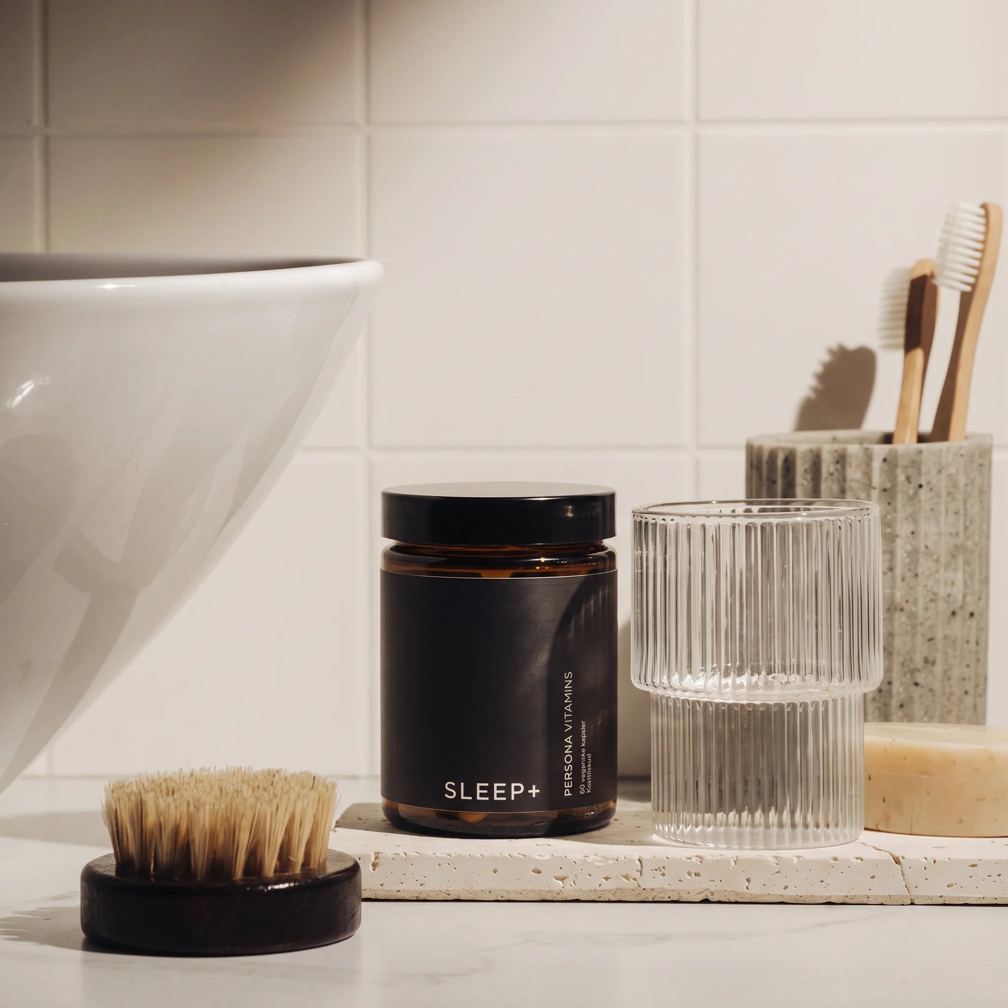 PersonaPath Sleep+ supplement jar on a stone tray in a bathroom, beside a ribbed glass and a bamboo toothbrush holder