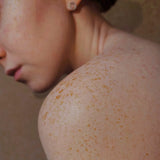 Close-up of a woman's freckled shoulder and neck, with her hair in a bun, photo by Valeria Smirnova
