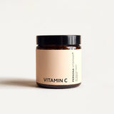 Amber glass jar with a black lid and a peach Vitamin C label on a cream background, front view in warm light